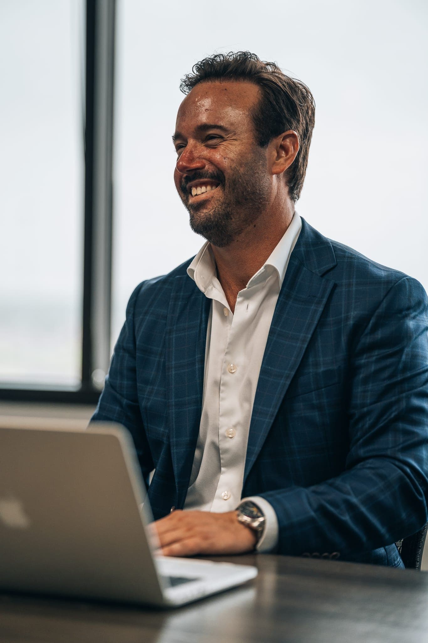 Jonathan Hawkins laughing at his desk in warm window light