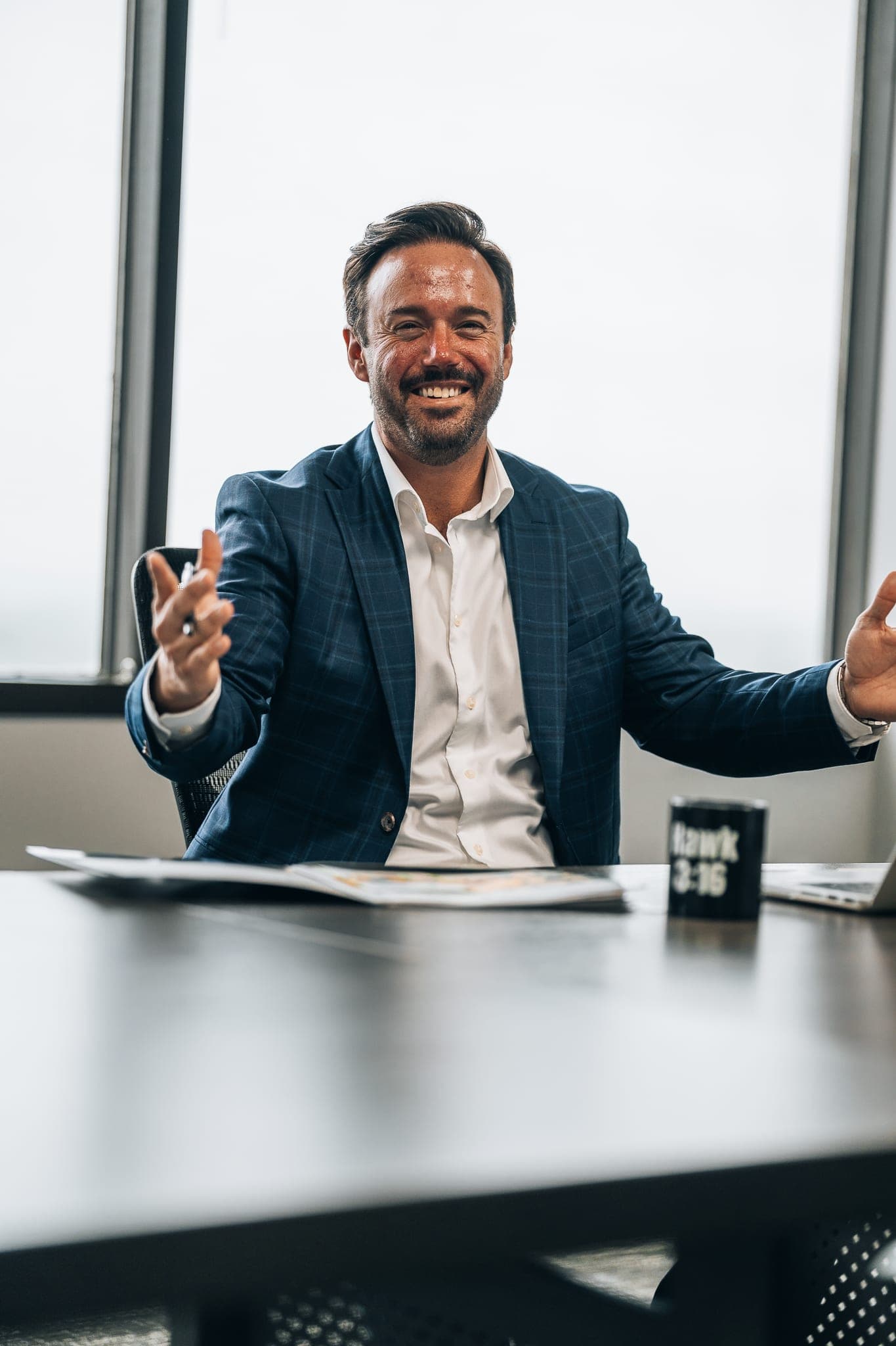 Jonathan Hawkins at his desk, arms open with a warm, welcoming smile